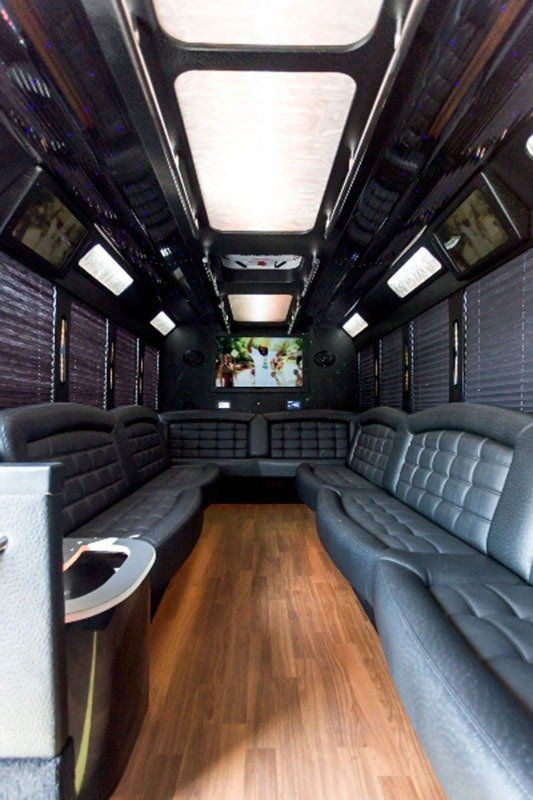 Interior of a black limousine with leather seating, wood floor, and TV screens.