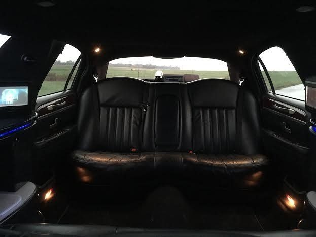 Interior of a black limousine with black leather seats and two small screens, with an outdoor view.