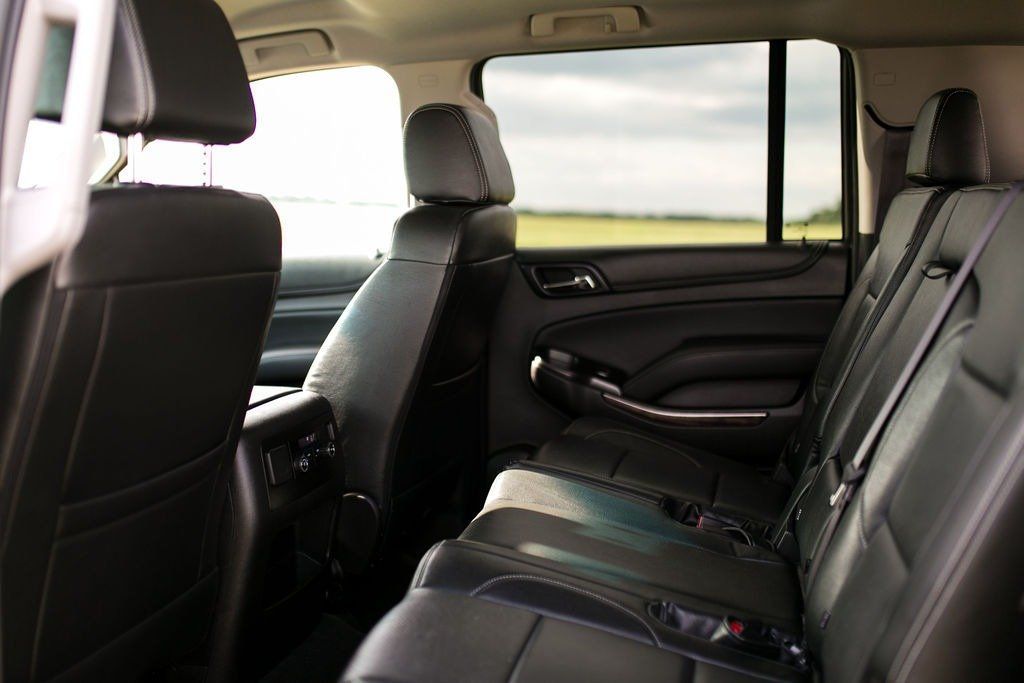 Interior of a black SUV with leather seats. Rear seats and headrests visible. Open window shows a field and sky.