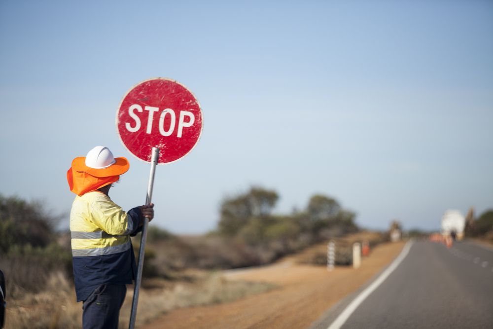 Worker Holding Stop Sign On Rural Road — Comprehensive Traffic Management in Cessnock, NSW