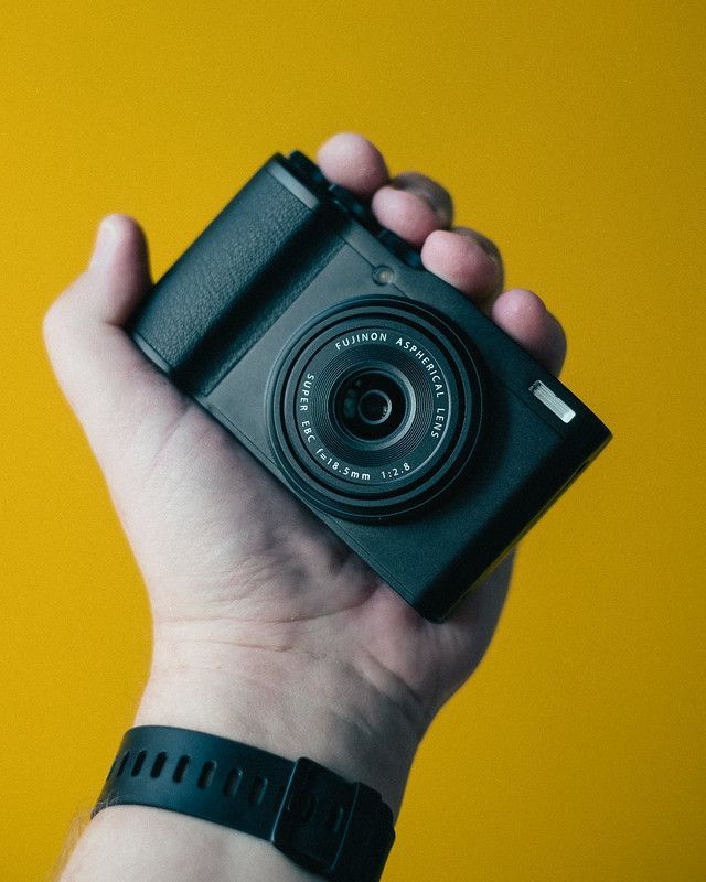 A person holding a black Fujifilm XF10 camera in their hand.