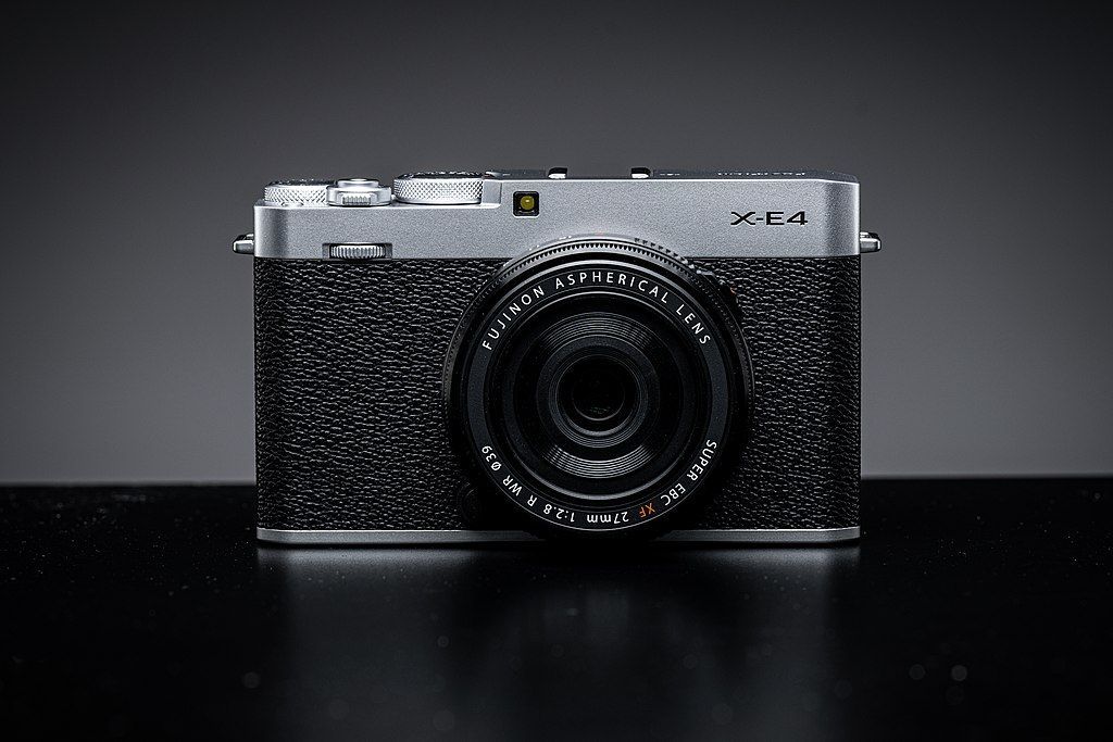 A black and silver fujifilm x-e4 camera sitting on a black table.