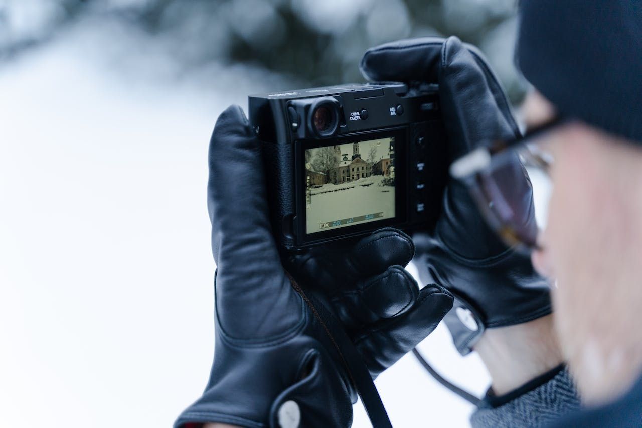 a person wearing gloves is taking a picture with a fujifilm x100v camera in the snow .