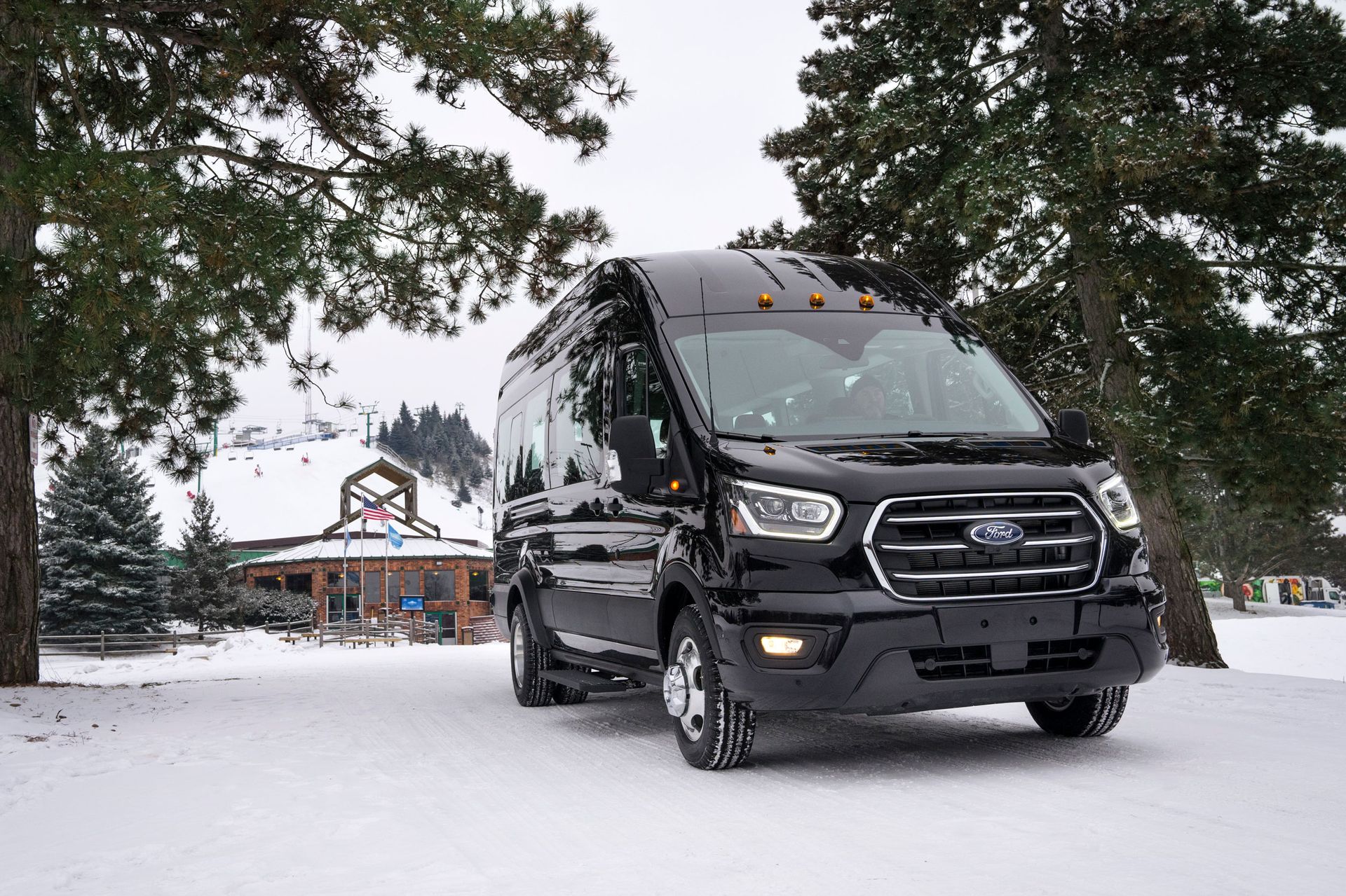 A black van is parked in the snow in front of a barn.