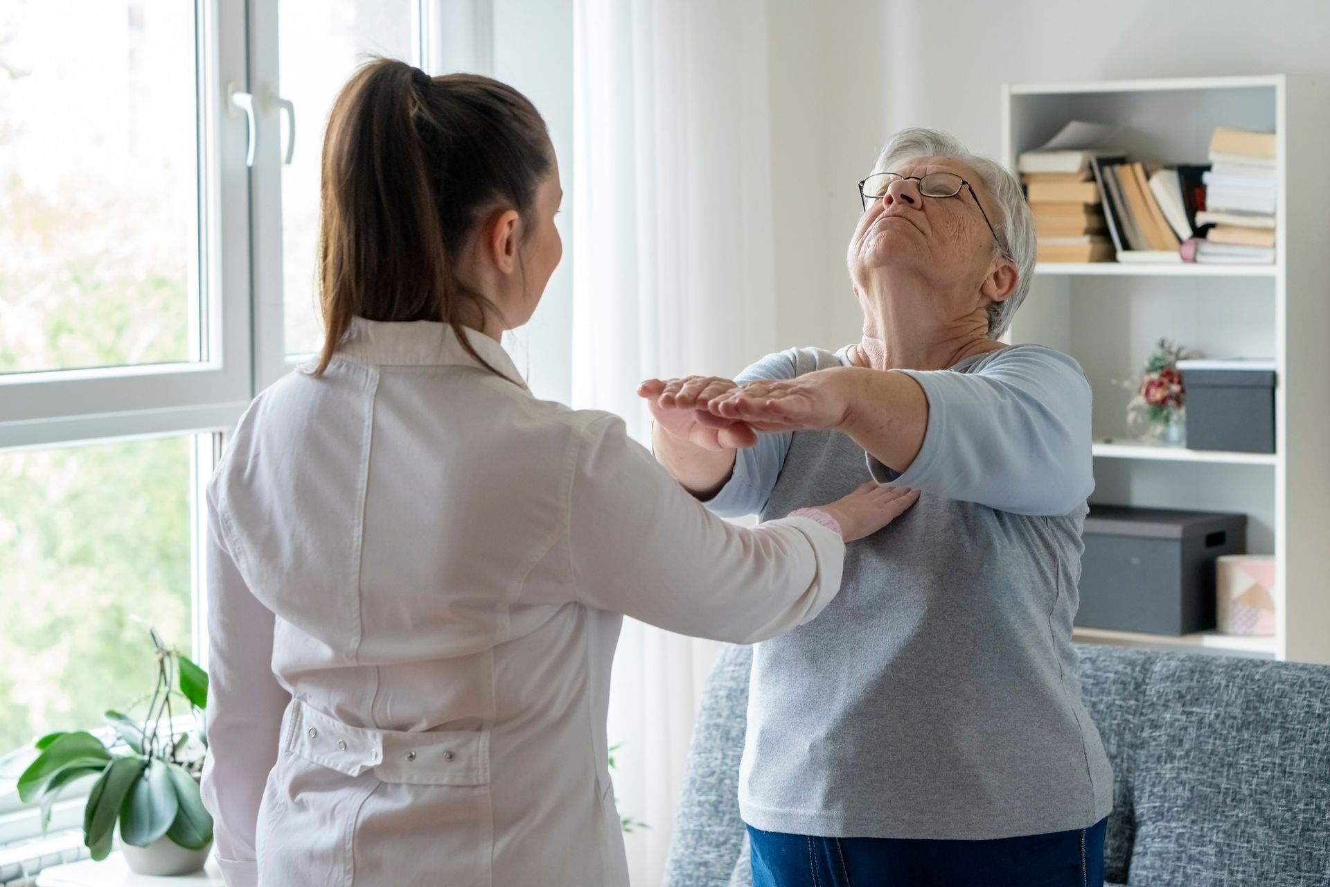 Un'infermiera in un centro di fisioterapia a Torino aiuta un'anziana signora a sgranchirsi le braccia in soggiorno.