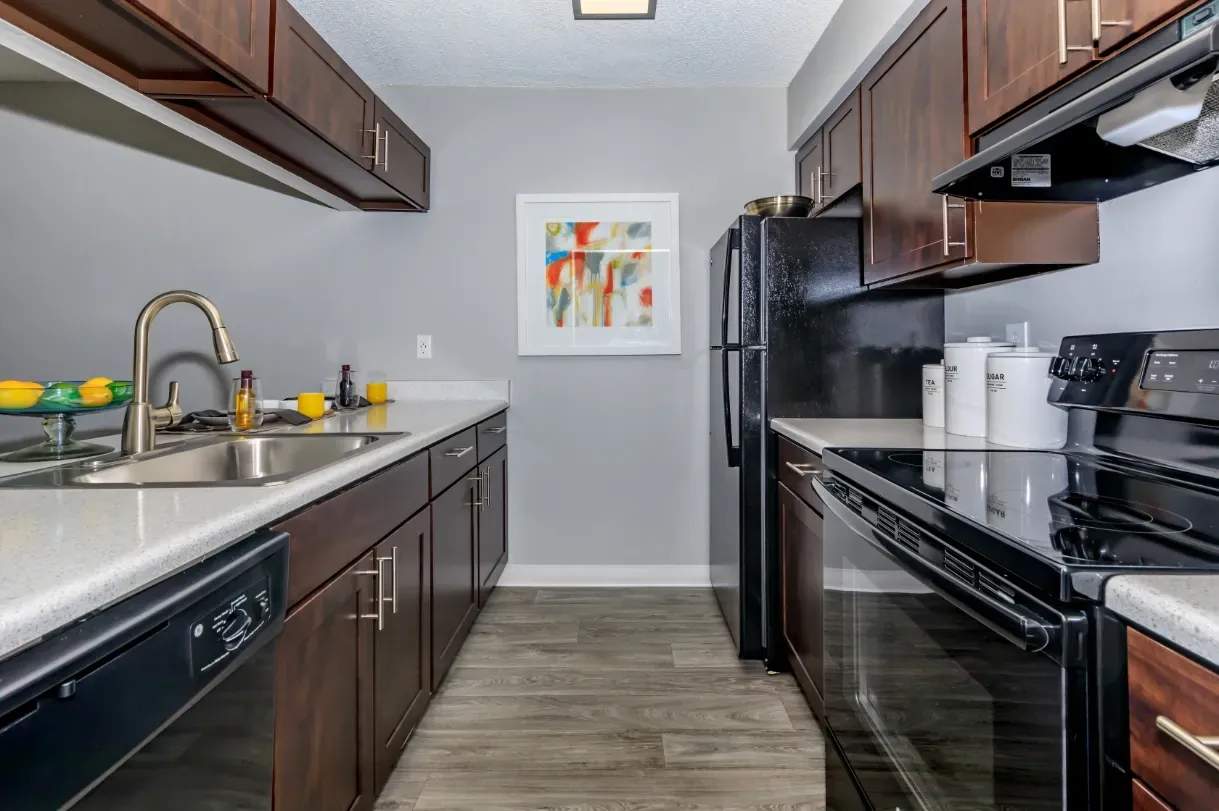 Kitchen with dark wood cabinets, white countertops, stainless steel sink, and black appliances.
