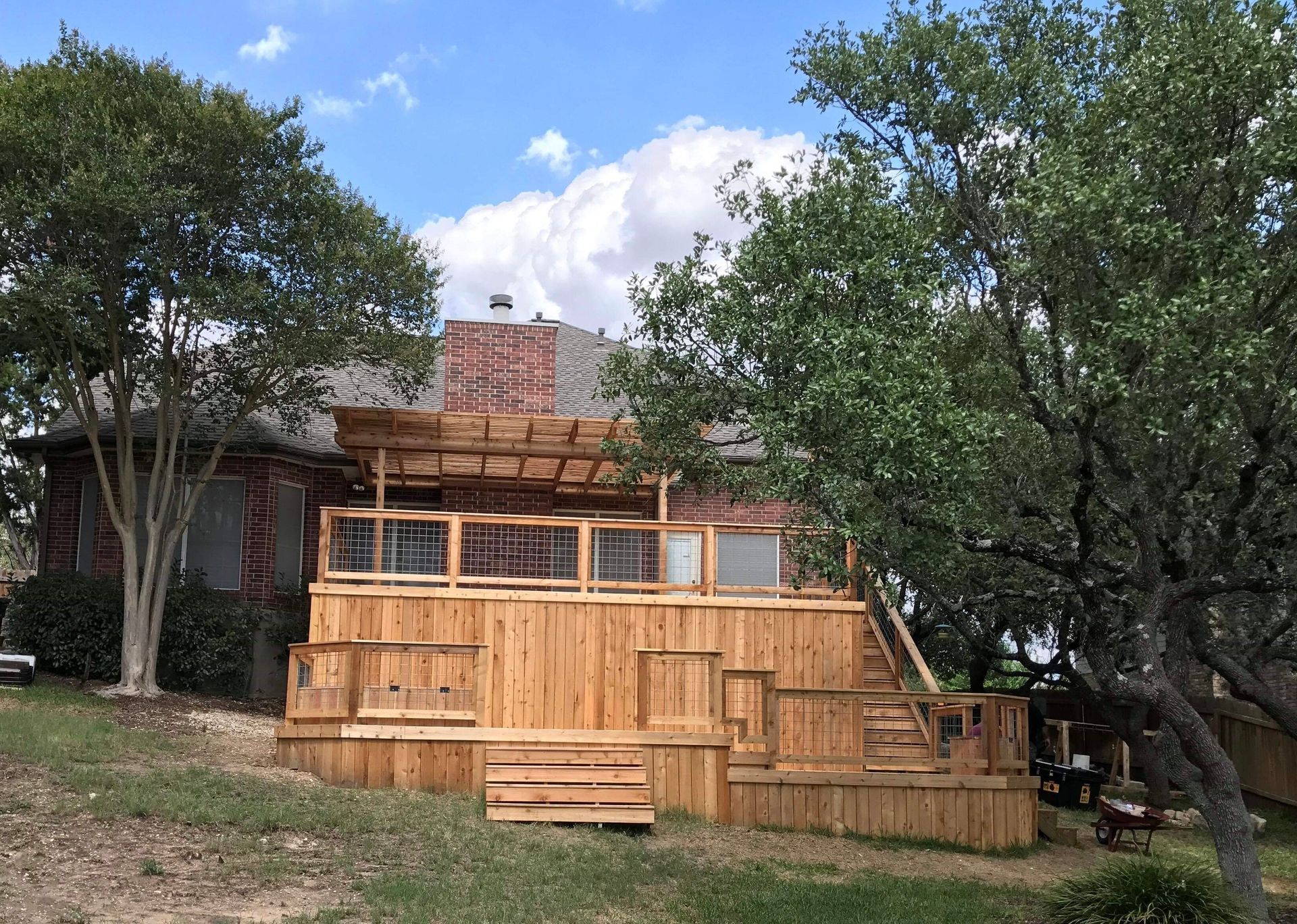 A large wooden deck is in front of a house surrounded by trees.