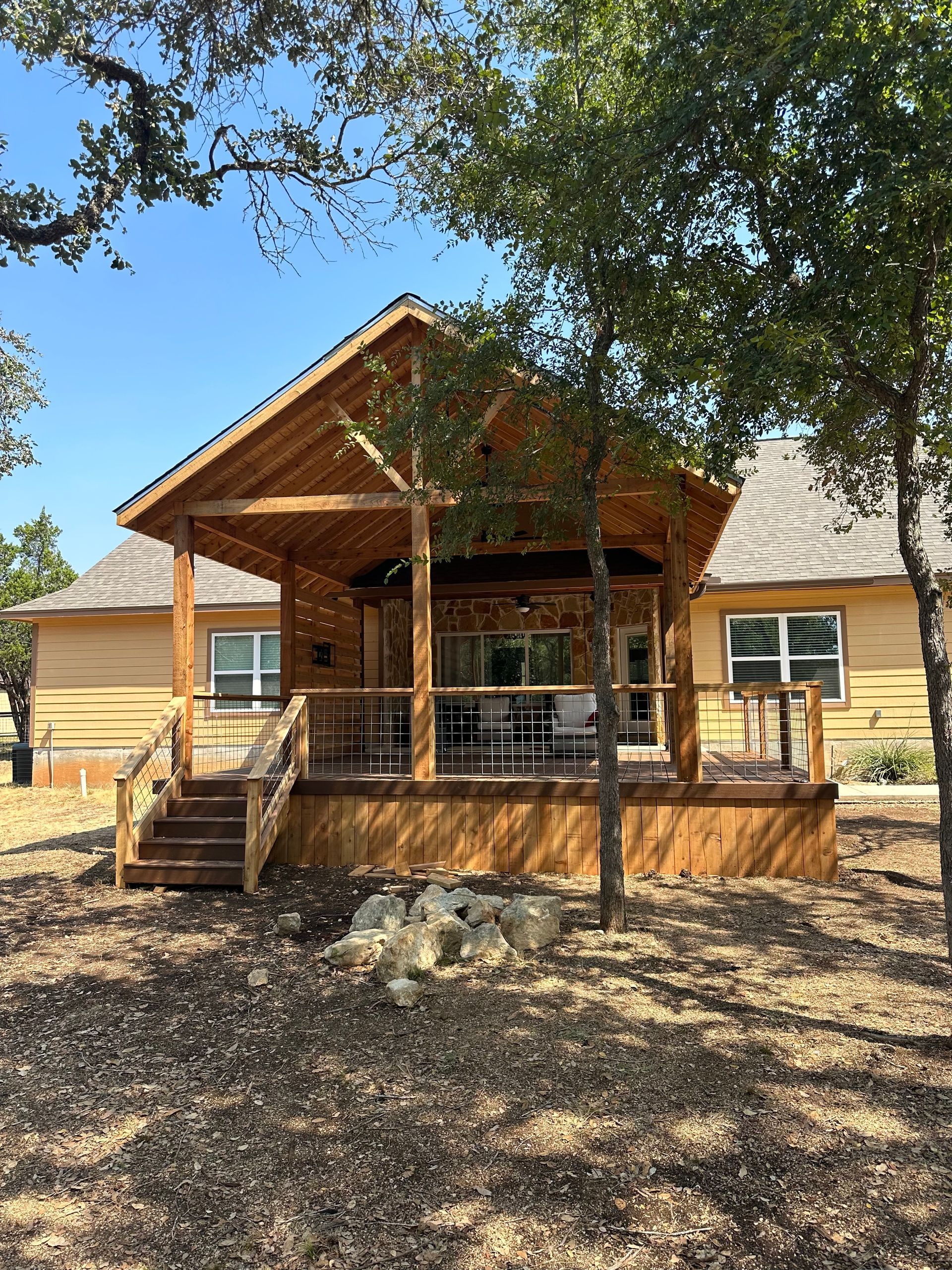 A small log cabin with a porch and stairs is surrounded by trees.