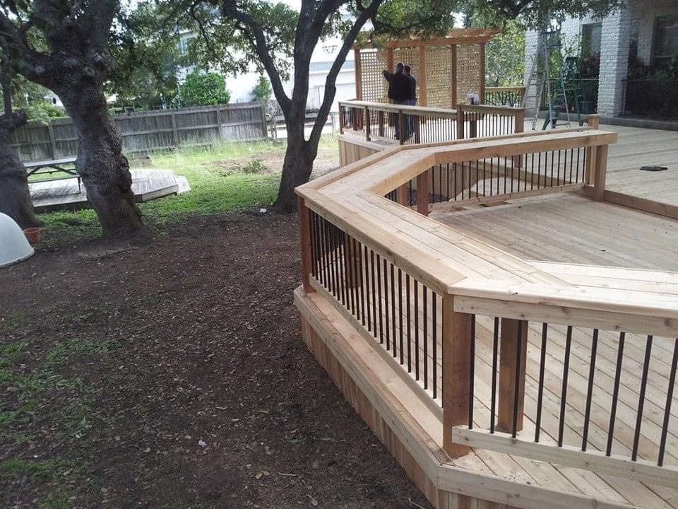 A wooden deck with a black railing is surrounded by trees