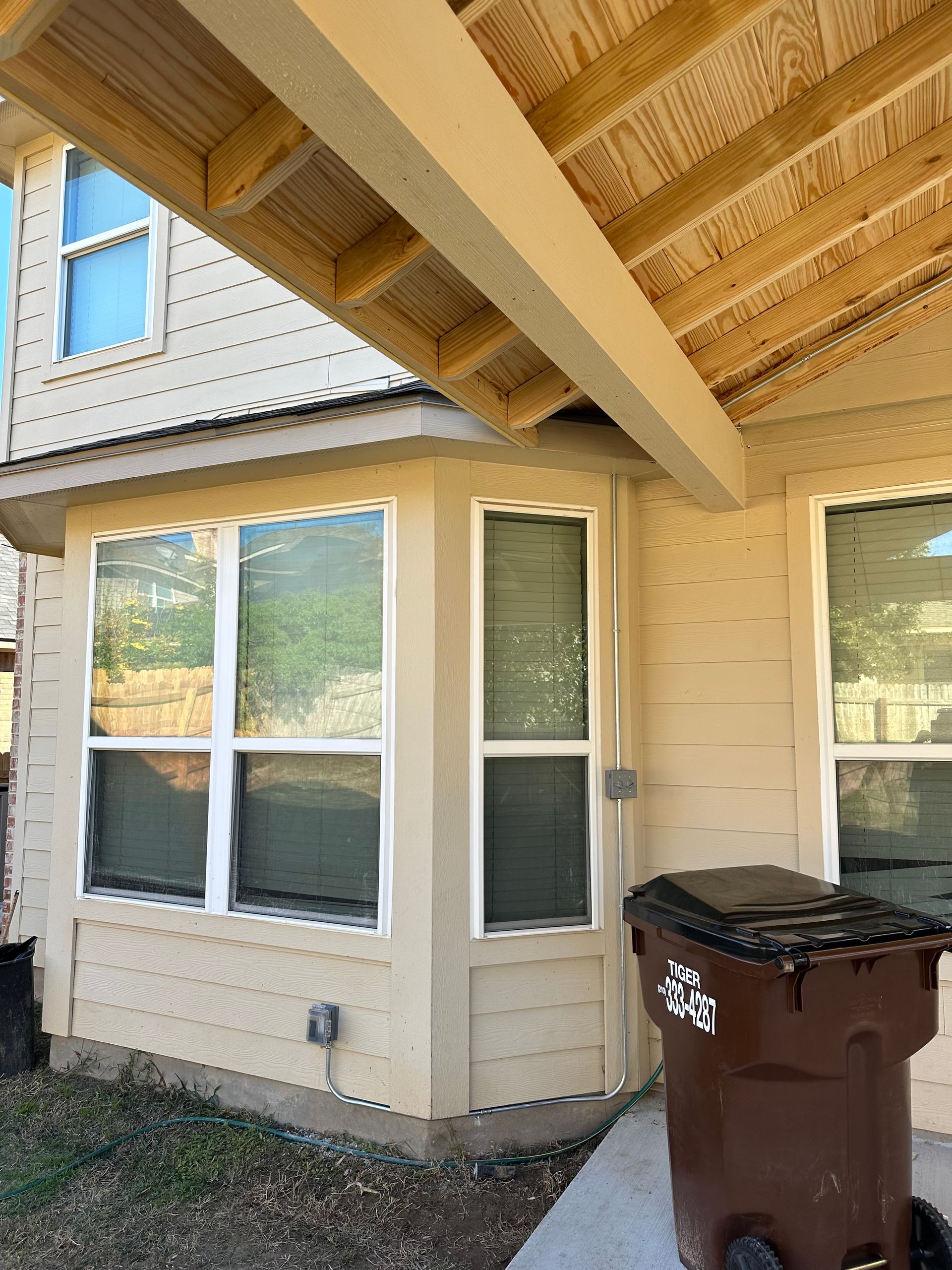 A brown trash can is parked in front of a house.