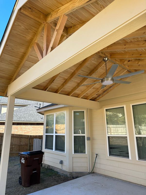 A covered patio with a ceiling fan and a trash can.