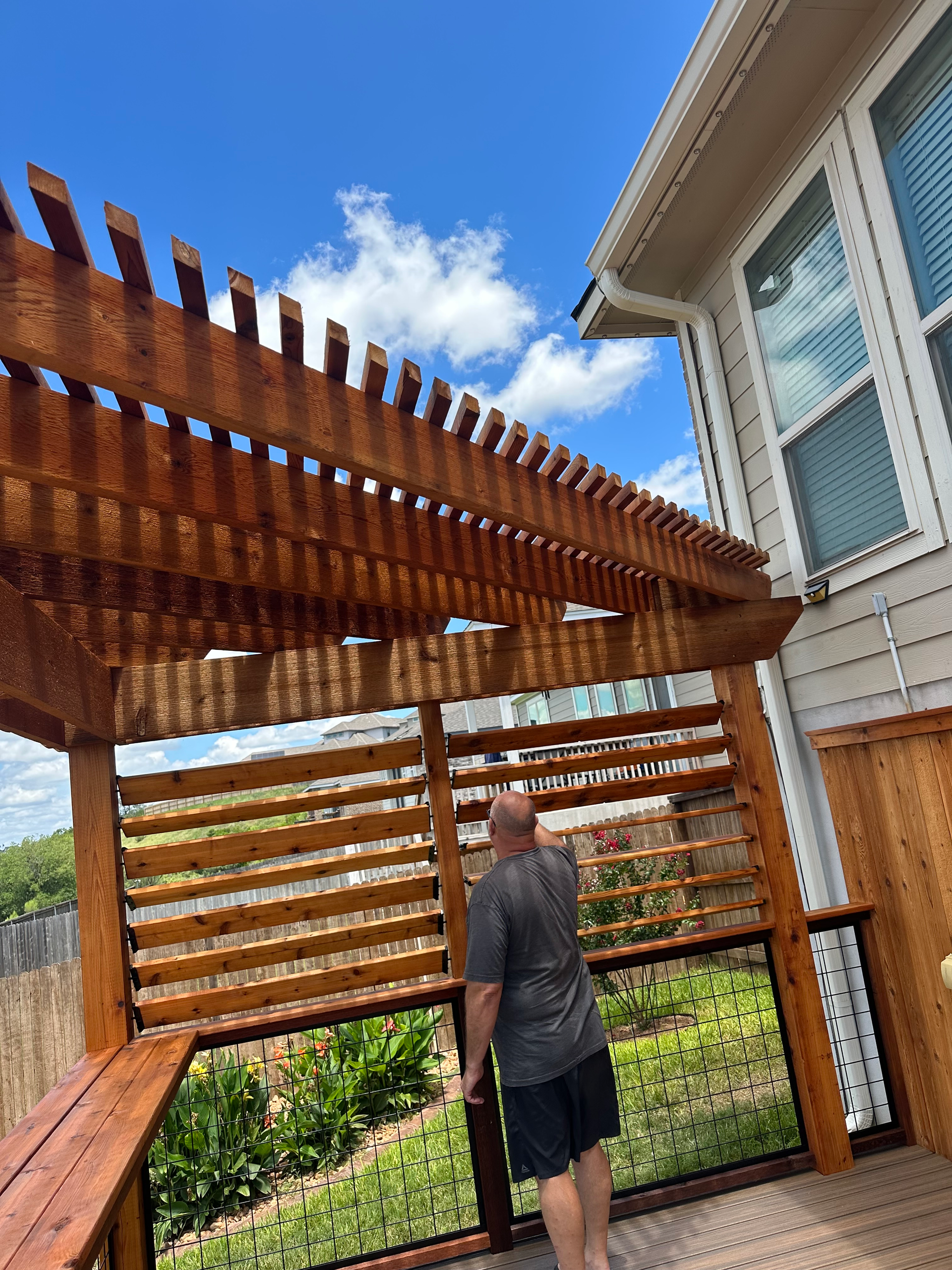 A man is standing on a deck under a wooden pergola.