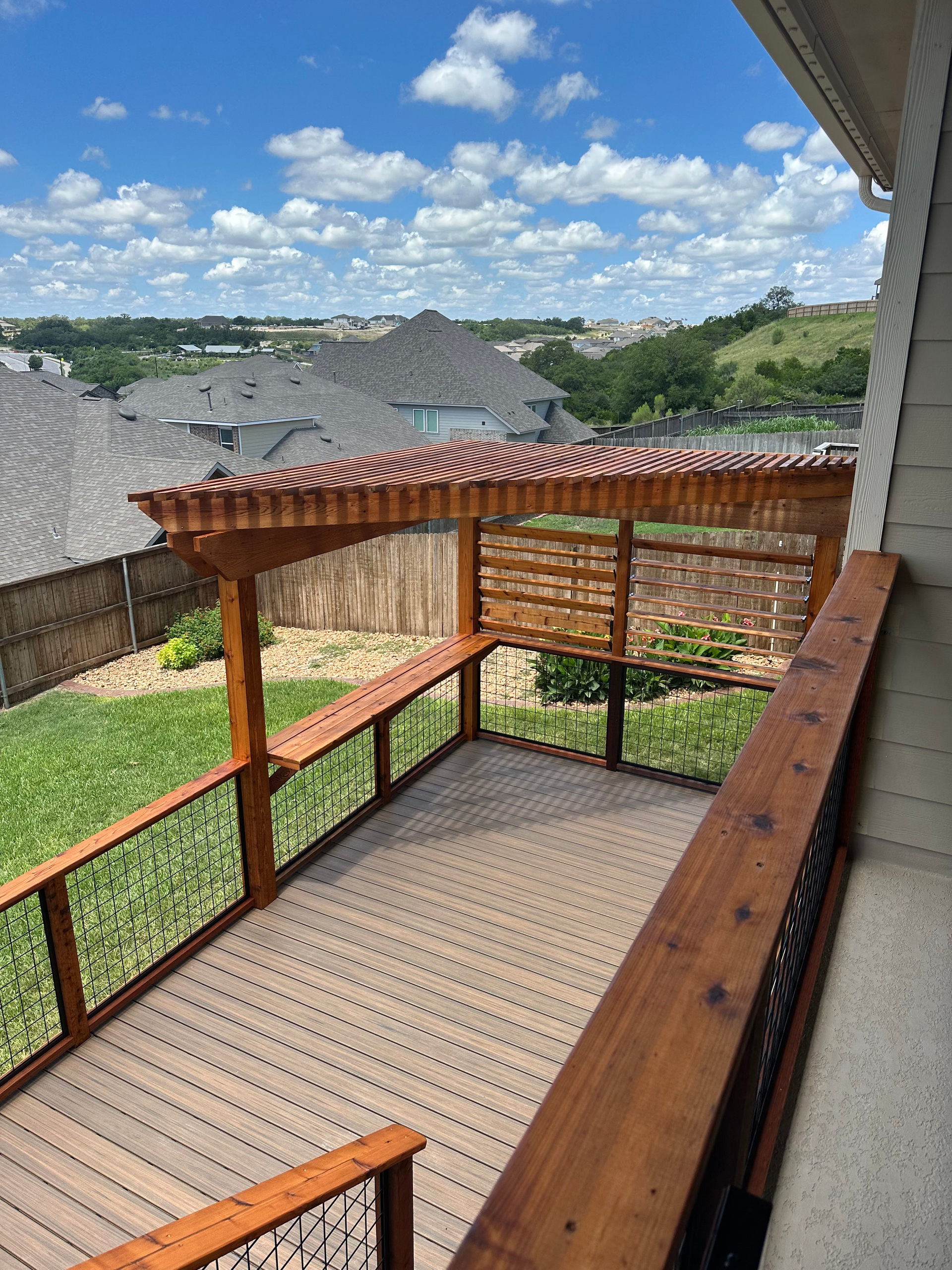 A wooden deck with a pergola and a view of the backyard.