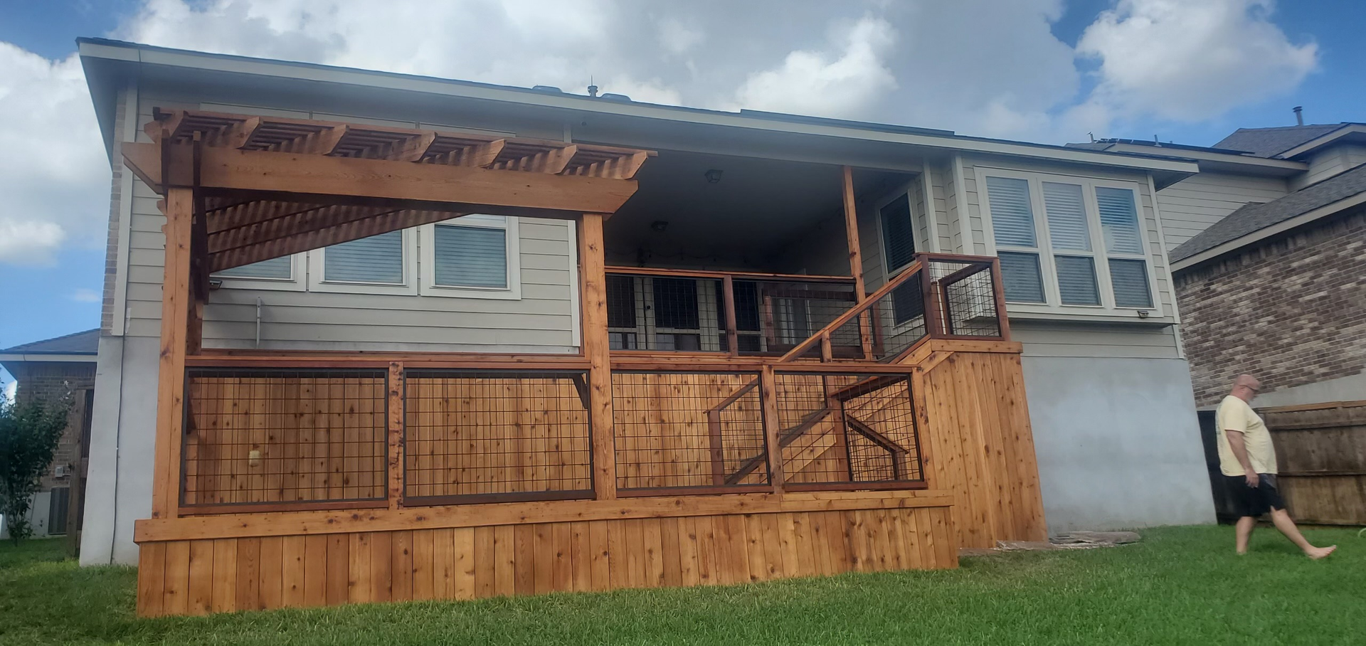 A man is walking in front of a house with a wooden deck.