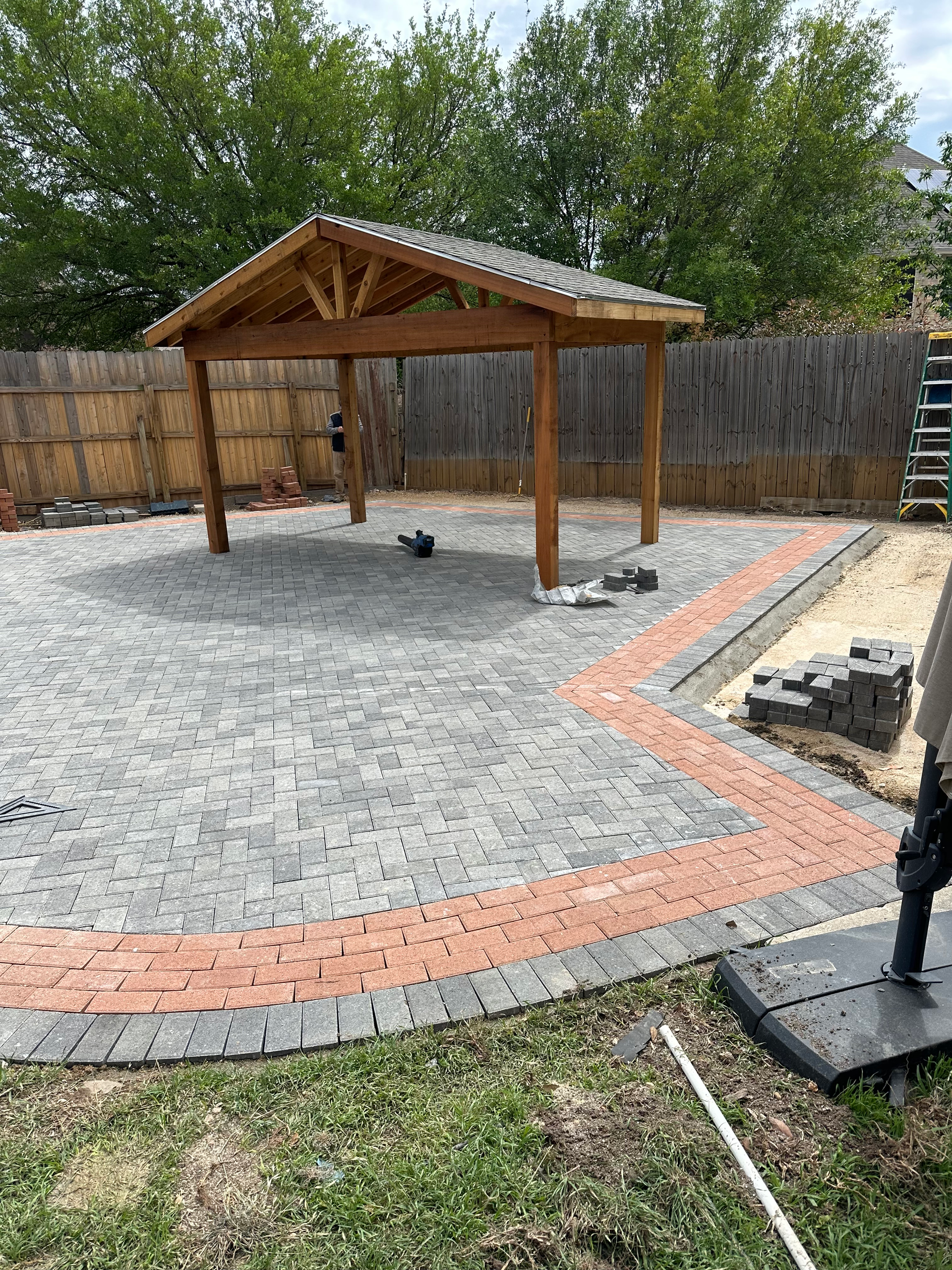 A man is working on a patio with a wooden gazebo.