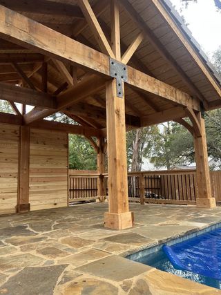 A wooden pavilion with a swimming pool in the background.