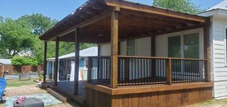 A wooden deck with a pergola over it is in front of a white house.