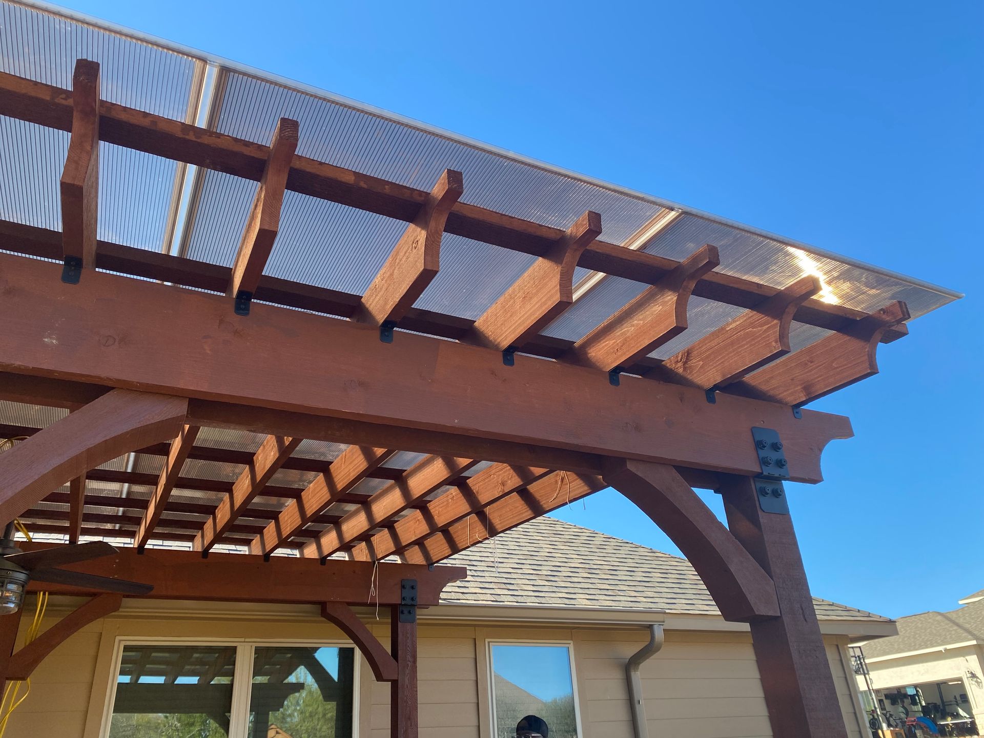 A wooden pergola with a clear roof is in front of a house.