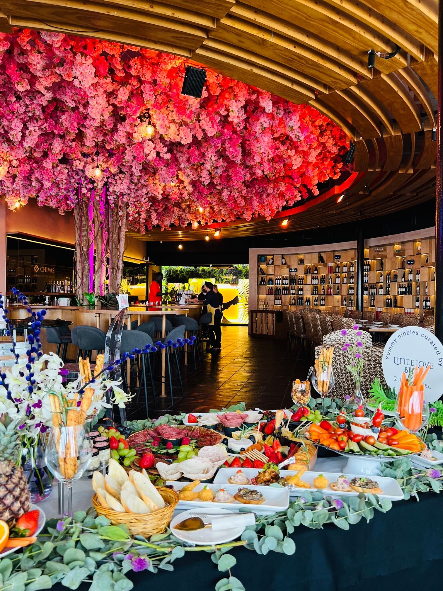 A buffet table in a restaurant with flowers hanging from the ceiling.