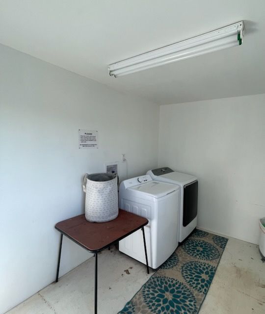 Laundry room: white appliances, table, basket, rug, fluorescent lighting.