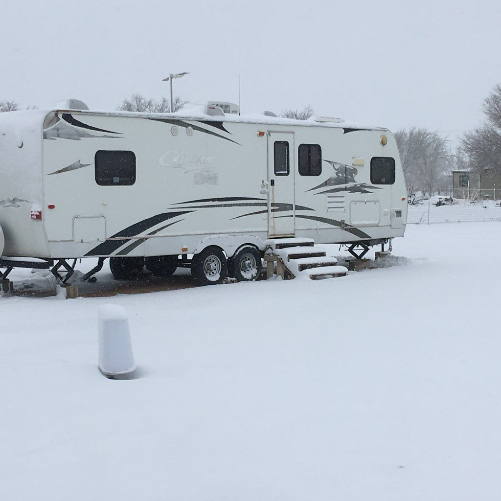 Camper covered in snow at a campsite. White with black accents. Snow covers the ground.