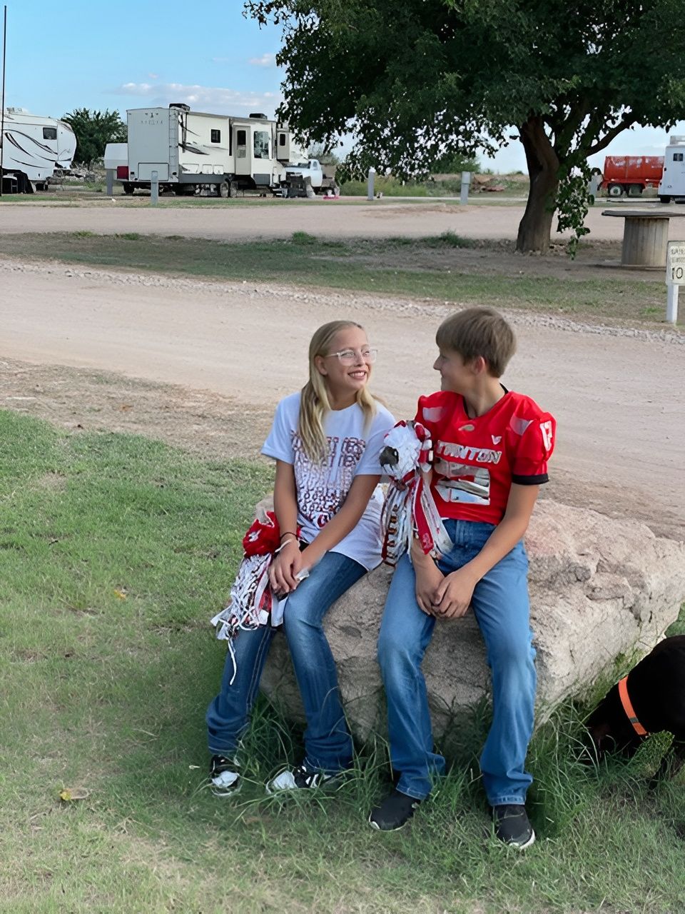 Two children seated on a rock at a campground, smiling at each other.