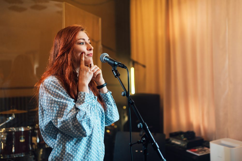 A woman is singing into a microphone in a recording studio.