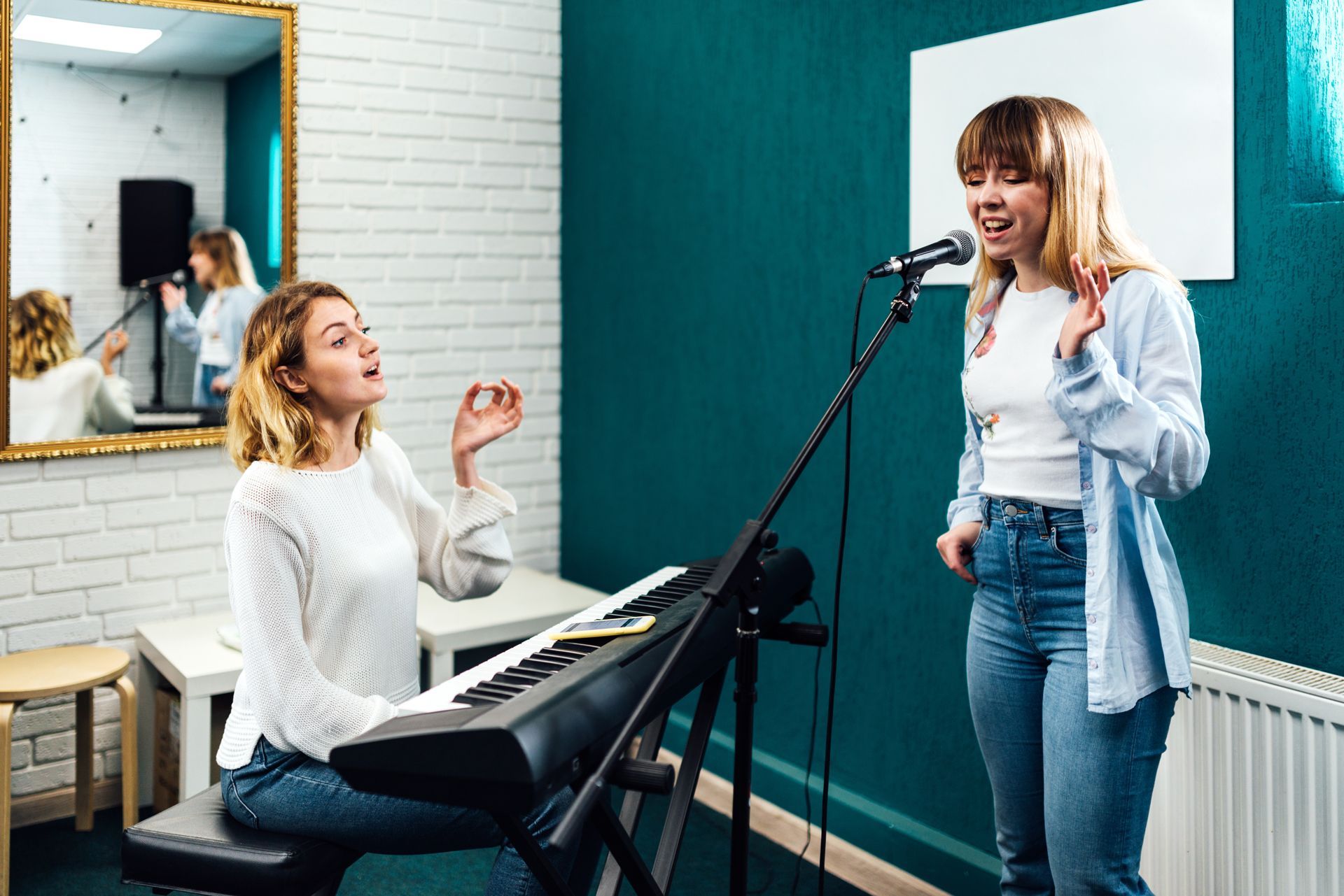 Two women are singing into microphones in a recording studio.