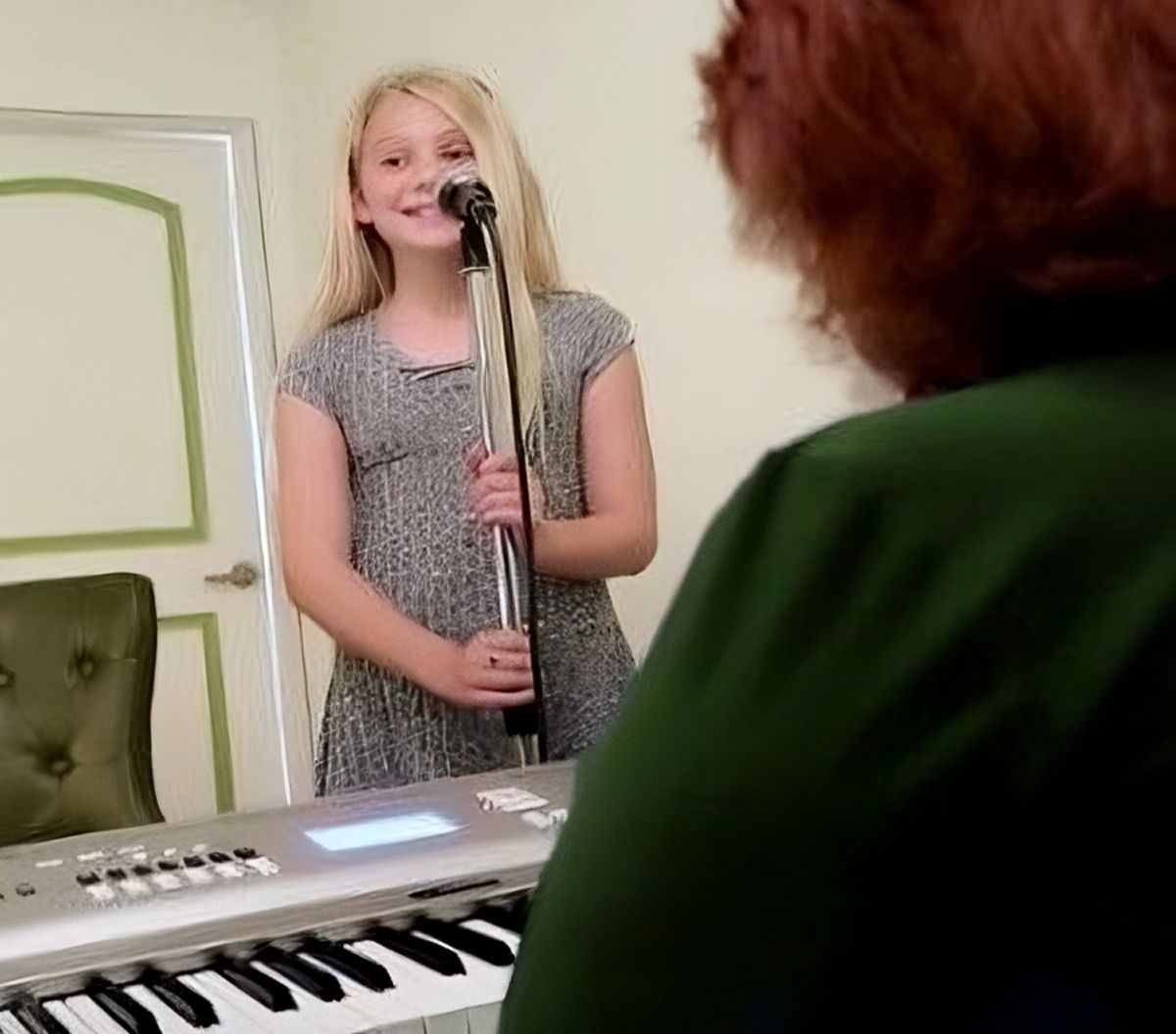 A young girl is singing into a microphone while playing a keyboard.