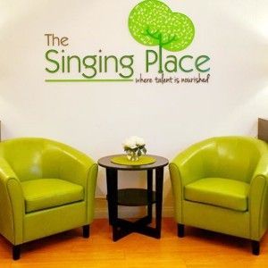 Two green chairs and a table in front of a wall that says the singing place