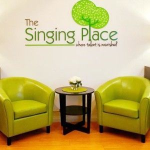 Two green chairs and a table in front of a wall that says the singing place
