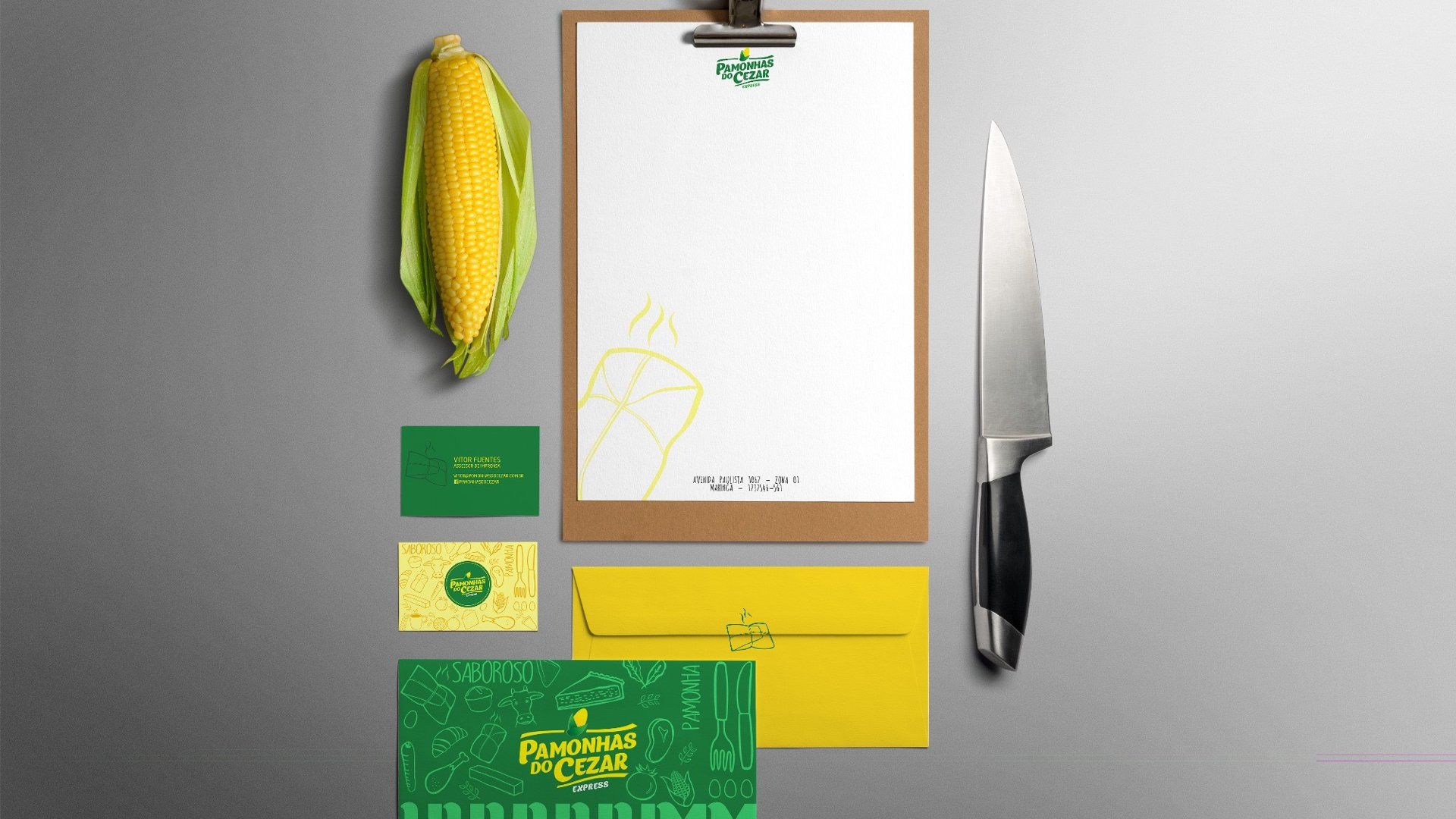 Conjunto de papelaria com milho, faca e logotipo em amarelo e verde sobre fundo cinza.