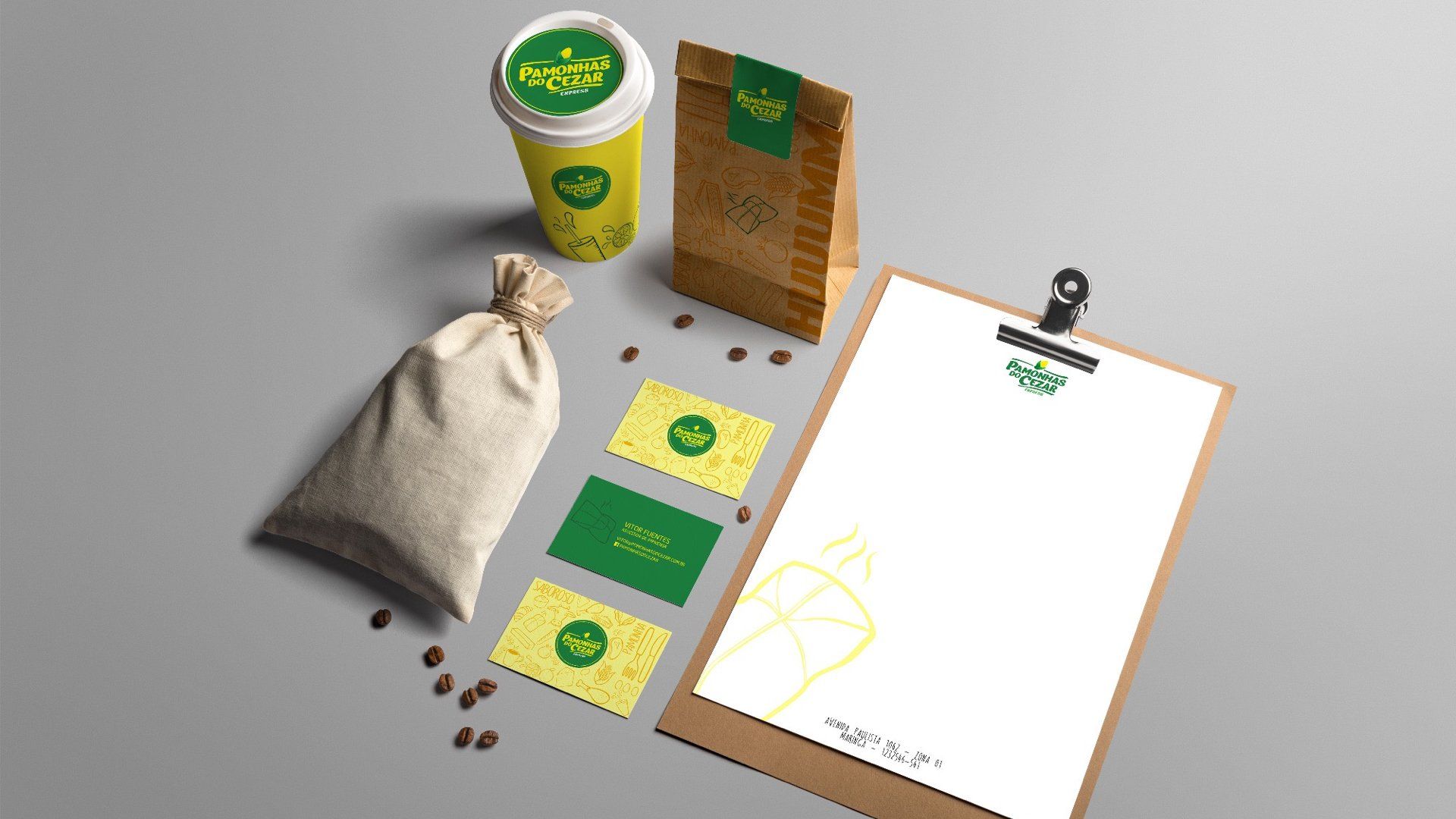 Modelo de marca com xícara de café, sacola, cartões de visita, prancheta e saco de grãos de café, tudo em verde e amarelo em uma superfície cinza.