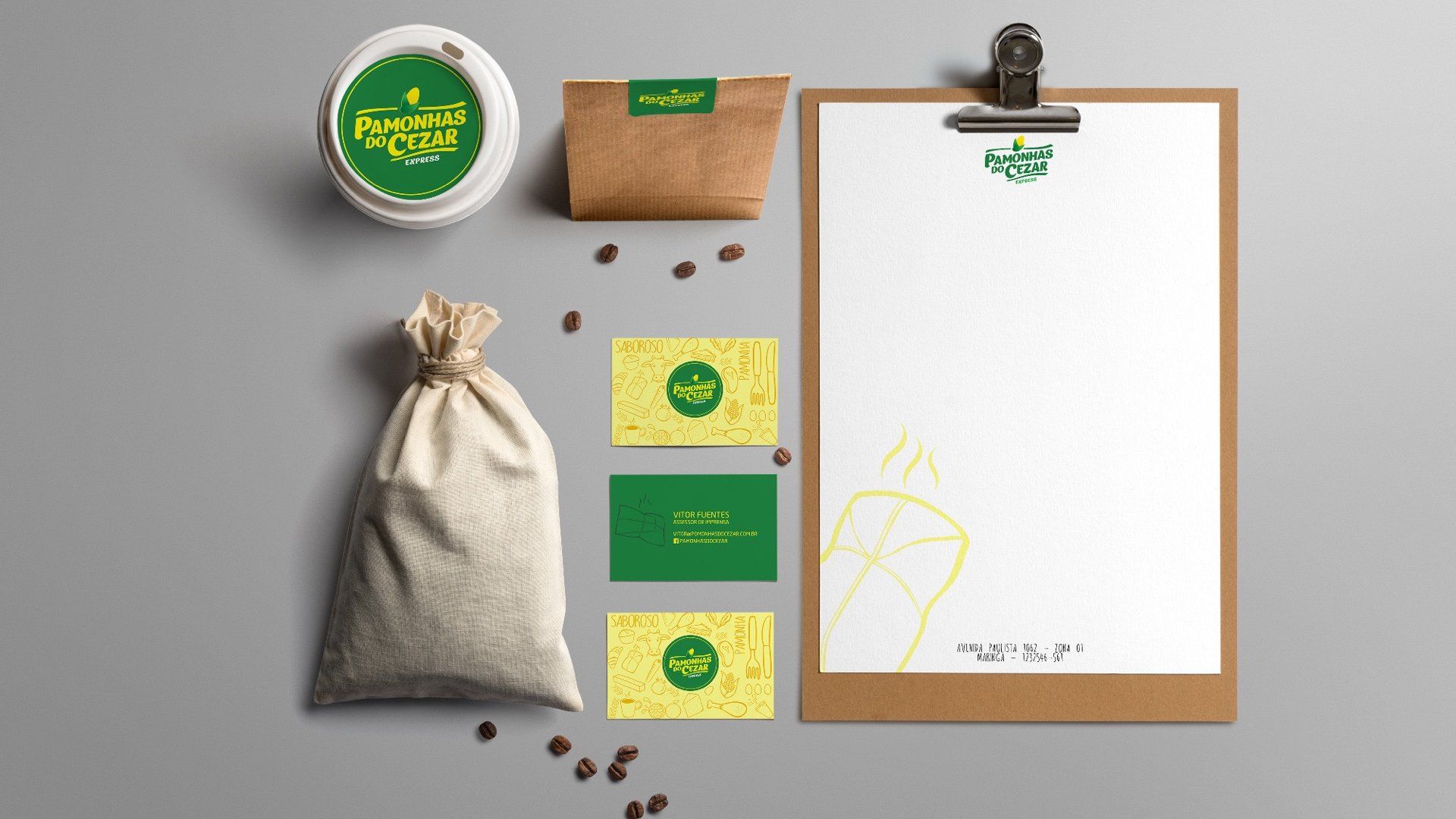 Layout plano da marca de café: lata, saco de estopa, cartões de visita, saco de papel, prancheta com papelaria e grãos de café em uma superfície cinza. Logotipo verde e amarelo.