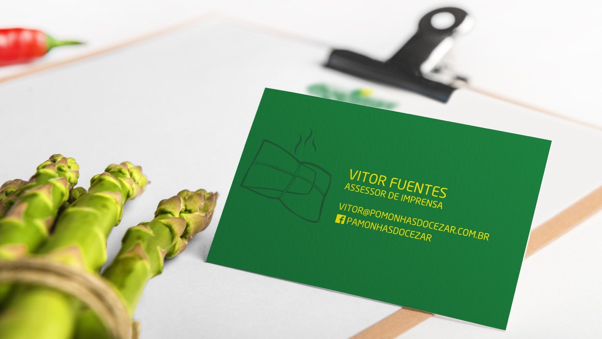 Cartão de visita verde com informações de contato ao lado de aspargos amarrados com barbante.