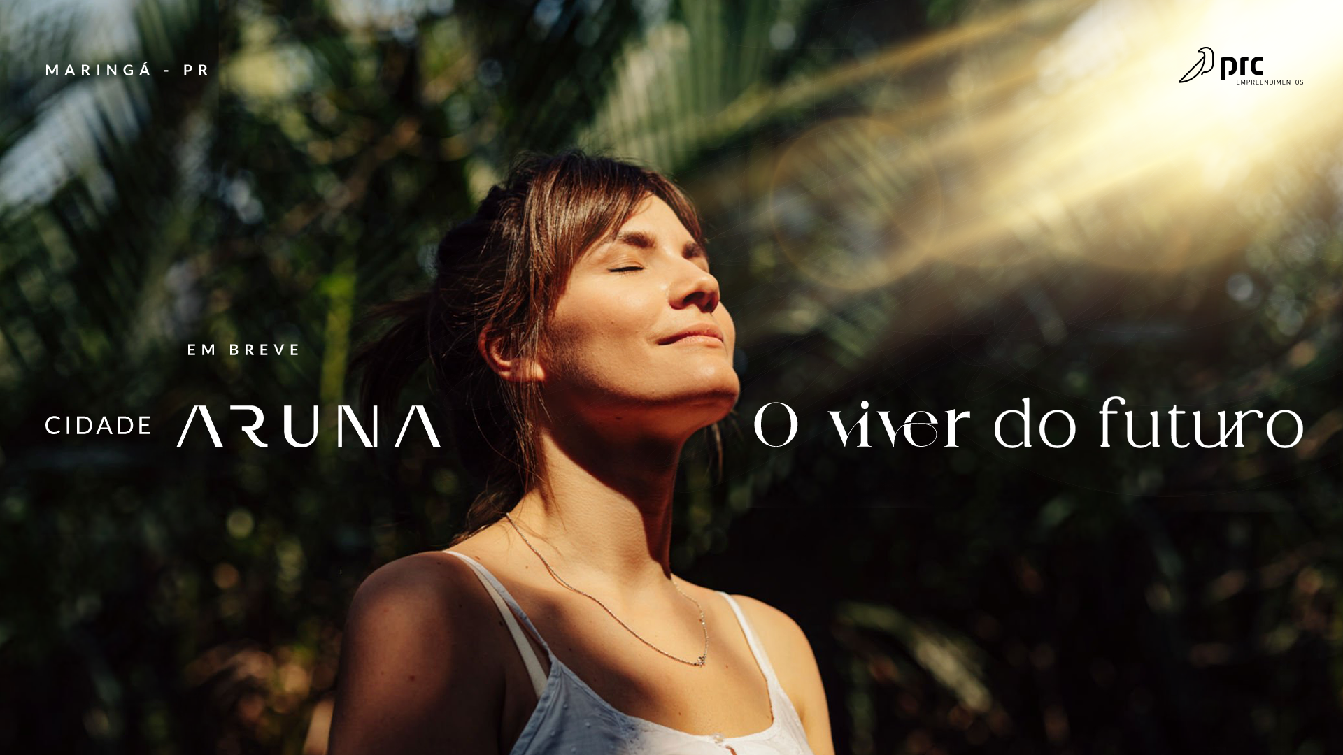 Mulher com os olhos fechados, banhada pela luz do sol, em frente à vegetação, escreve