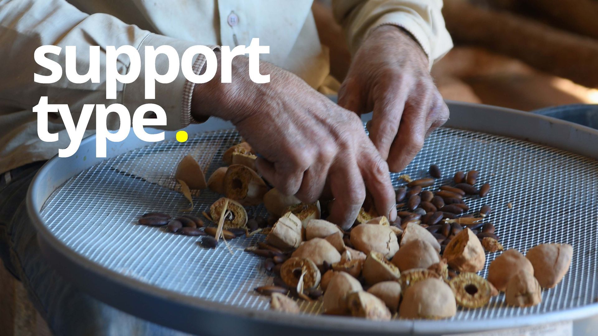 Mãos separando nozes e sementes em uma peneira de metal.