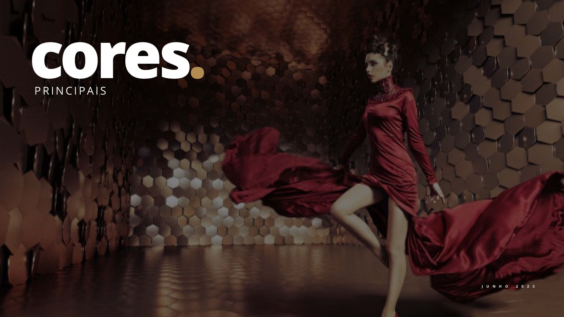 Uma mulher de vestido vermelho posa em frente a uma parede metálica abstrata. A palavra