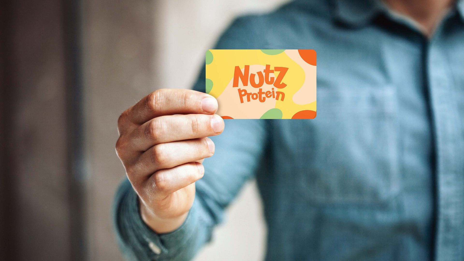 Pessoa de camisa azul segurando um cartão-presente da Nutz Protein, que tem um design laranja e verde.