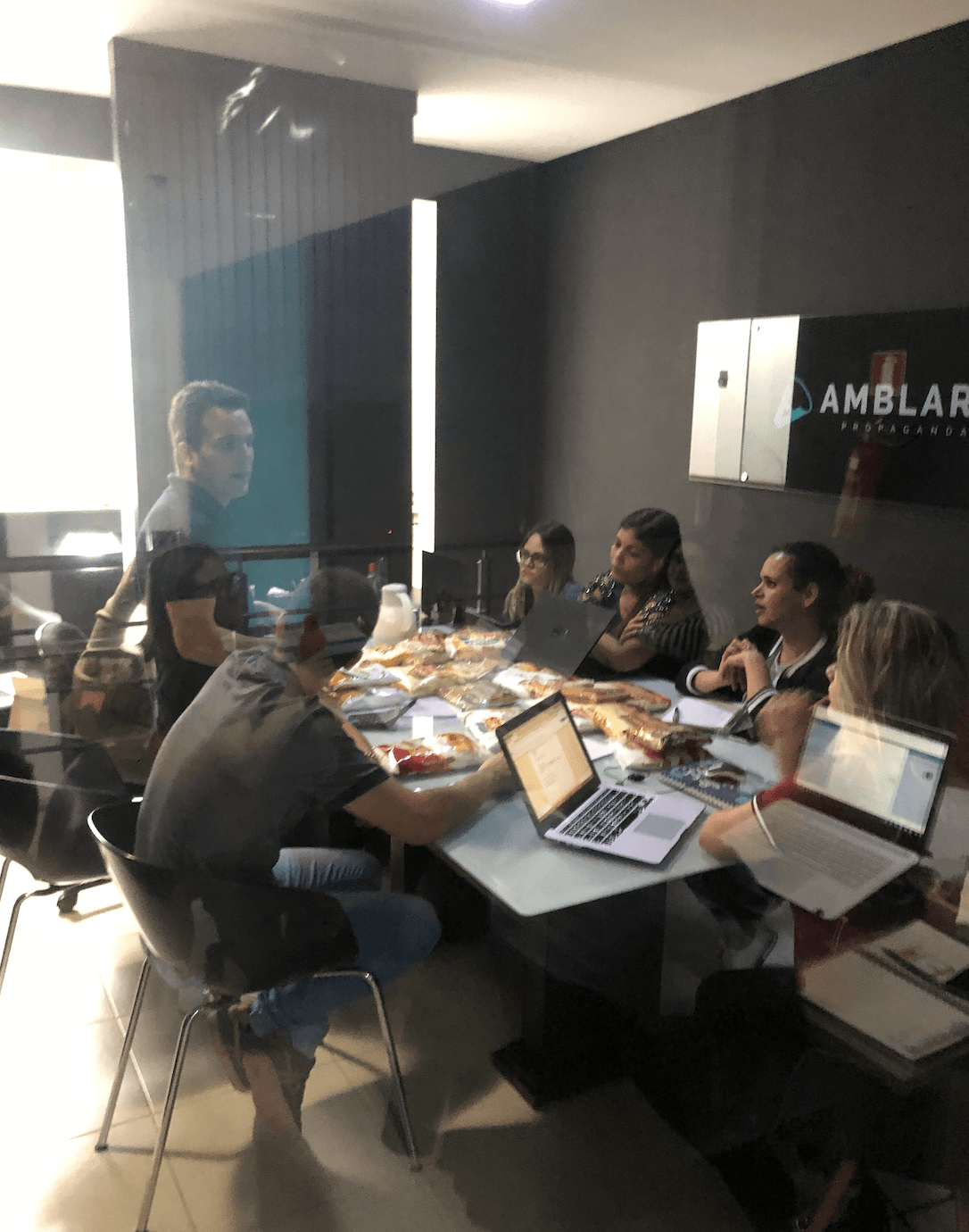 Um grupo de pessoas reunidas ao redor de uma mesa em um escritório moderno, trabalhando em laptops e documentos durante uma reunião.