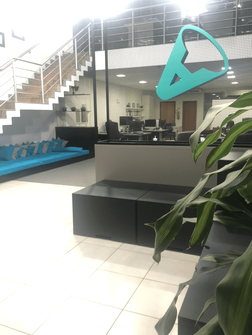 Interior de escritório moderno com uma área de espera com um banco azul acolchoado, uma escada e um logotipo na parede de vidro.