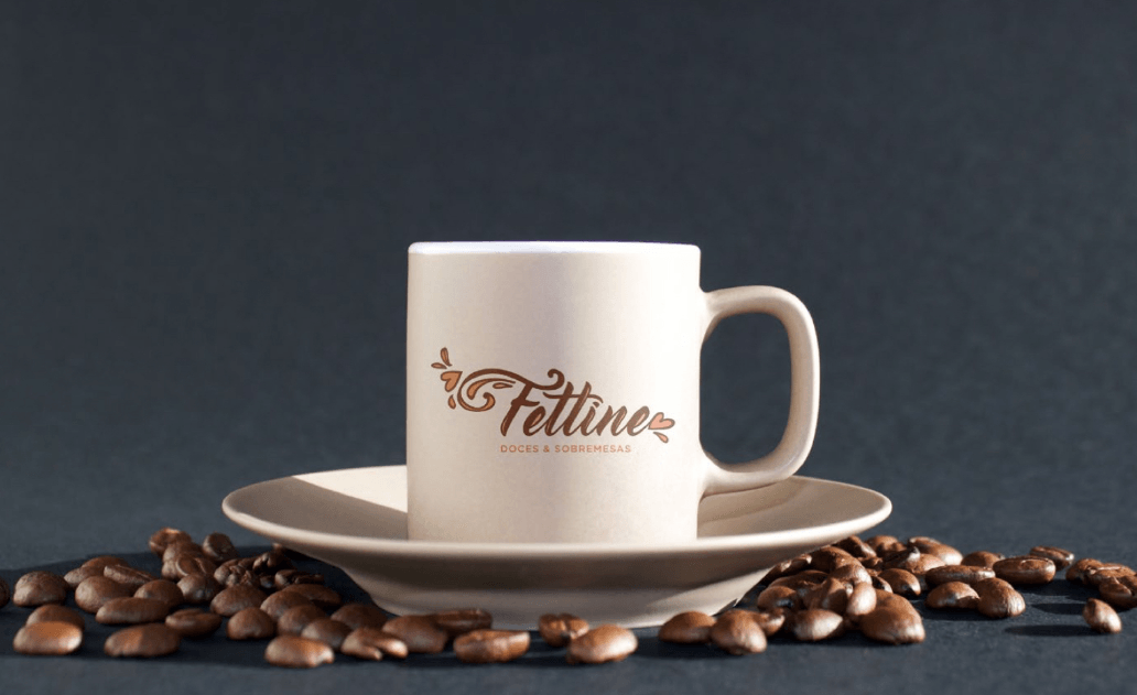 Xícara de café branca sobre um pires com grãos de café espalhados. A xícara tem o logotipo
