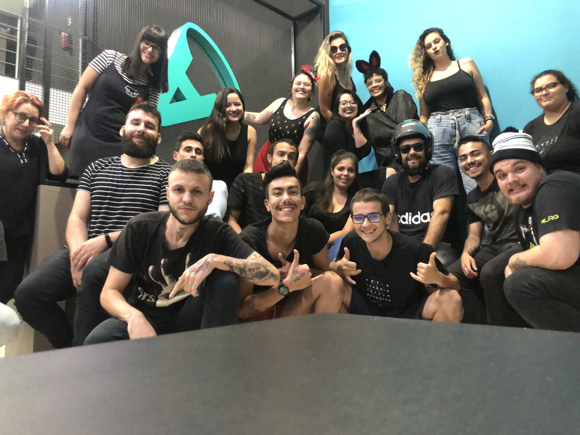 Grupo de pessoas sorrindo para a câmera. A maioria vestida de preto, em frente a uma parede turquesa e cinza.