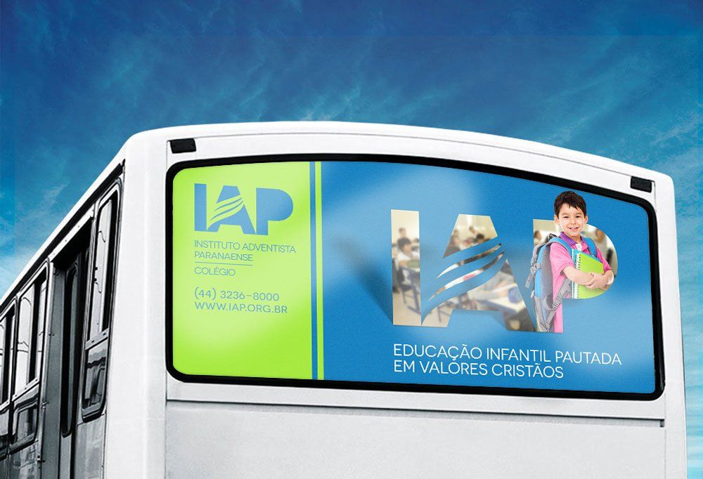 Vista traseira de um ônibus com um anúncio da escola IAP. O anúncio tem fundo verde e azul, a foto de um aluno e o texto
