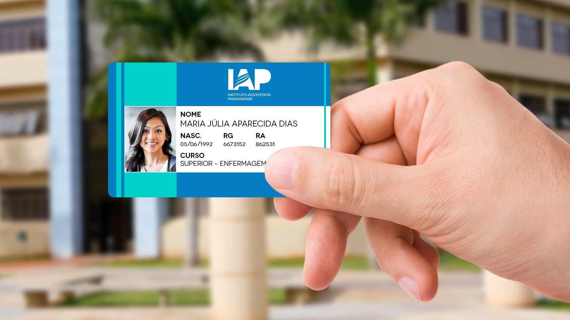 Mão segurando um documento de identidade com a foto de uma mulher, contra um fundo desfocado. O cartão tem as cores azul e verde-azulado.