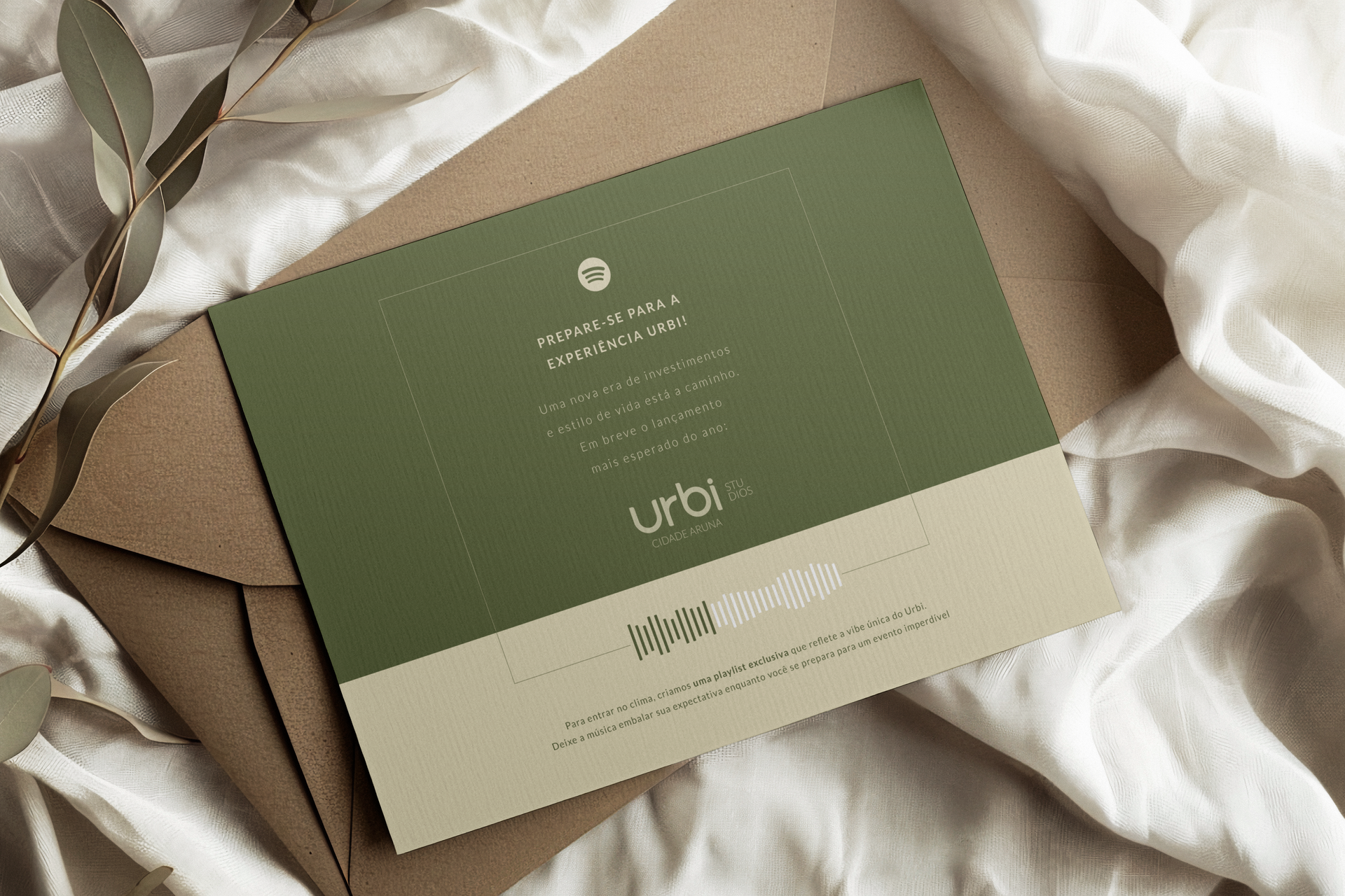 Um cartão dobrado verde-oliva e bege com texto, sobre um envelope marrom, sobre um pano branco amassado.