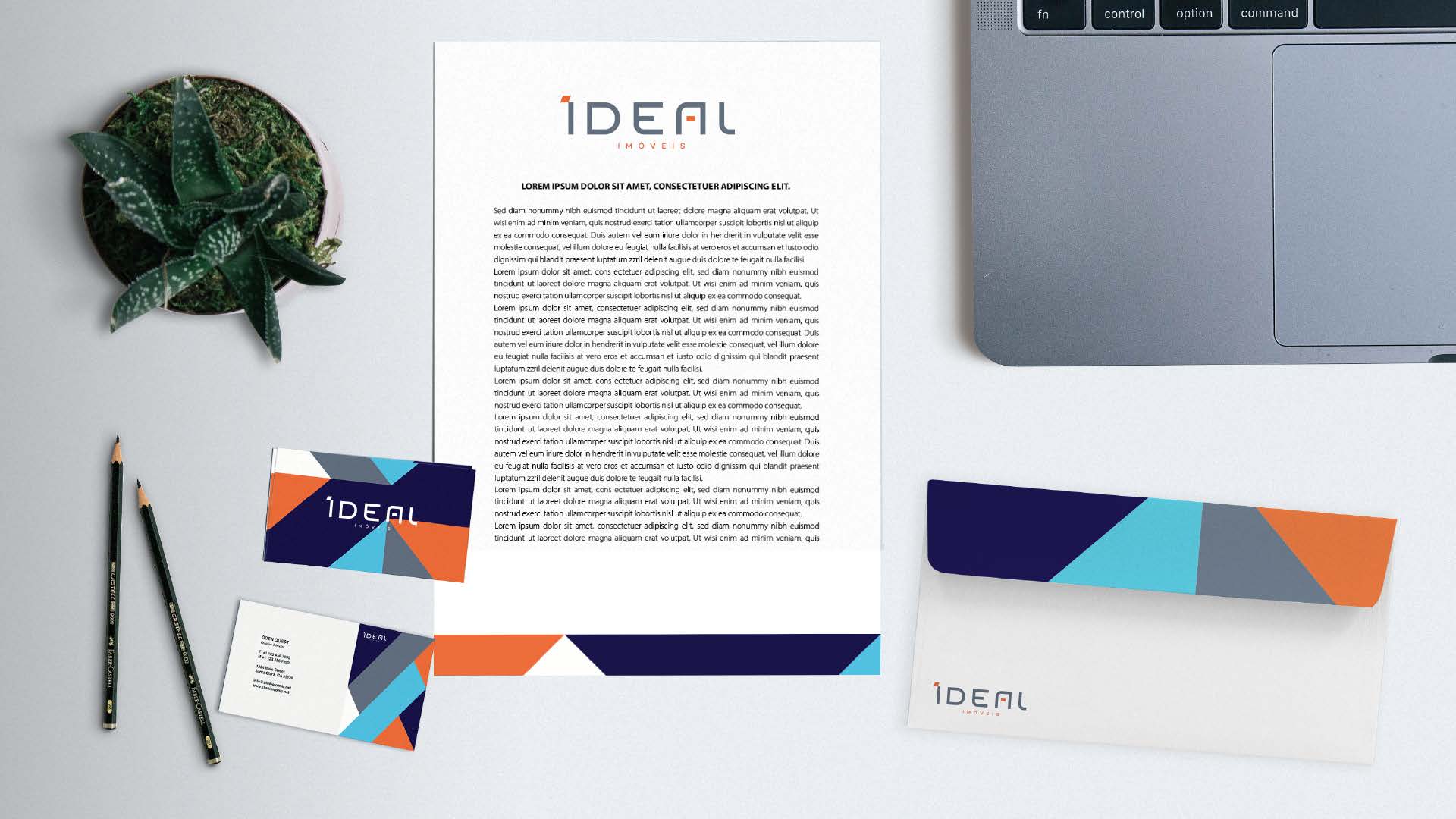 Material de escritório personalizado sobre uma mesa, incluindo papel timbrado, cartões de visita e envelope, além de um laptop, uma planta e lápis.