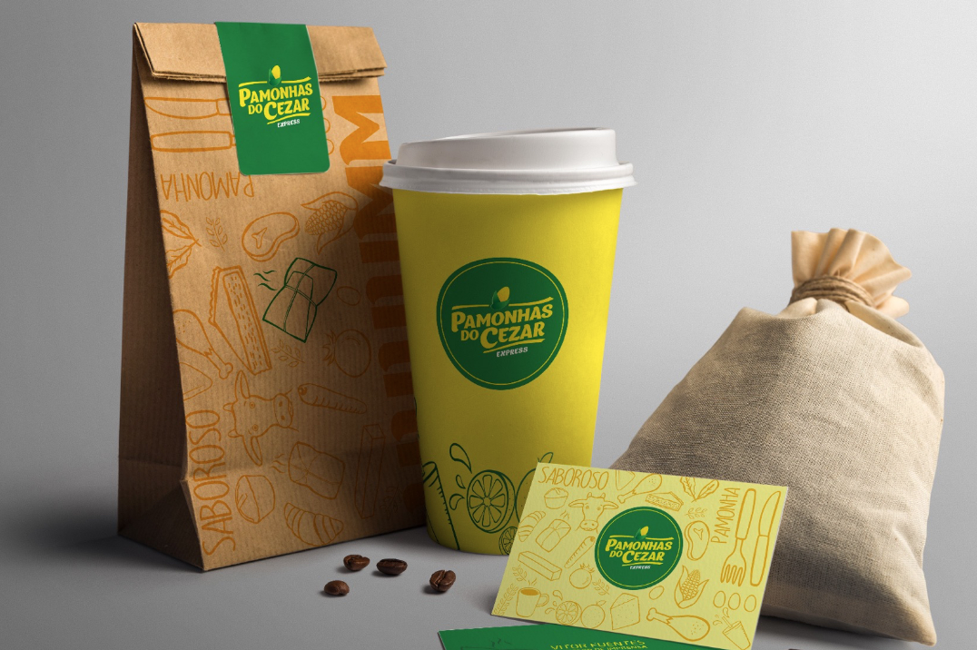 Embalagem de café: um saco de papel, um copo, um saco de estopa e um cartão de visita, todos com um logotipo verde e amarelo. Grãos de café espalhados.