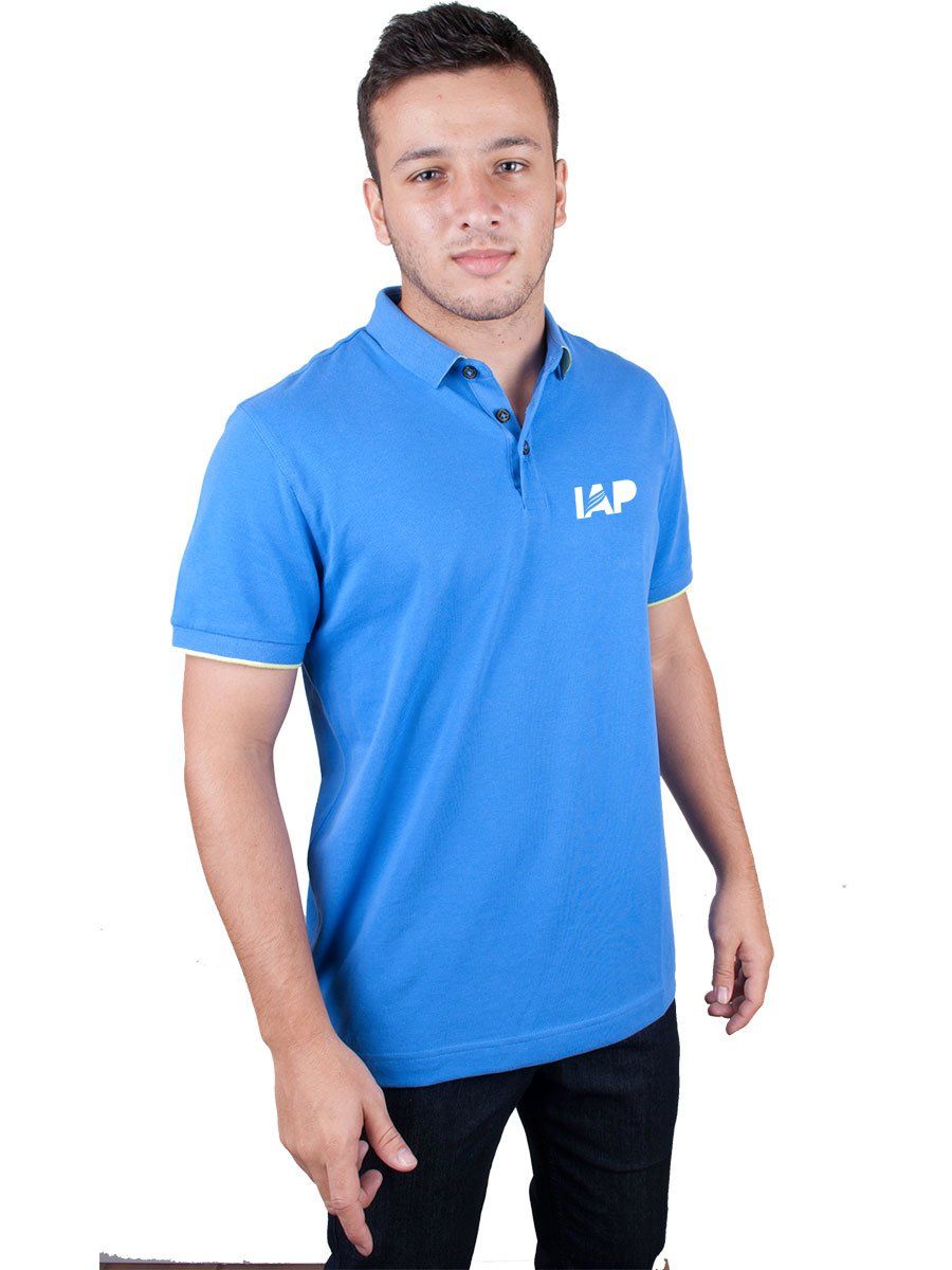 Homem vestindo uma camisa polo azul com logotipo, em pé, com expressão neutra. Ele veste calças escuras.