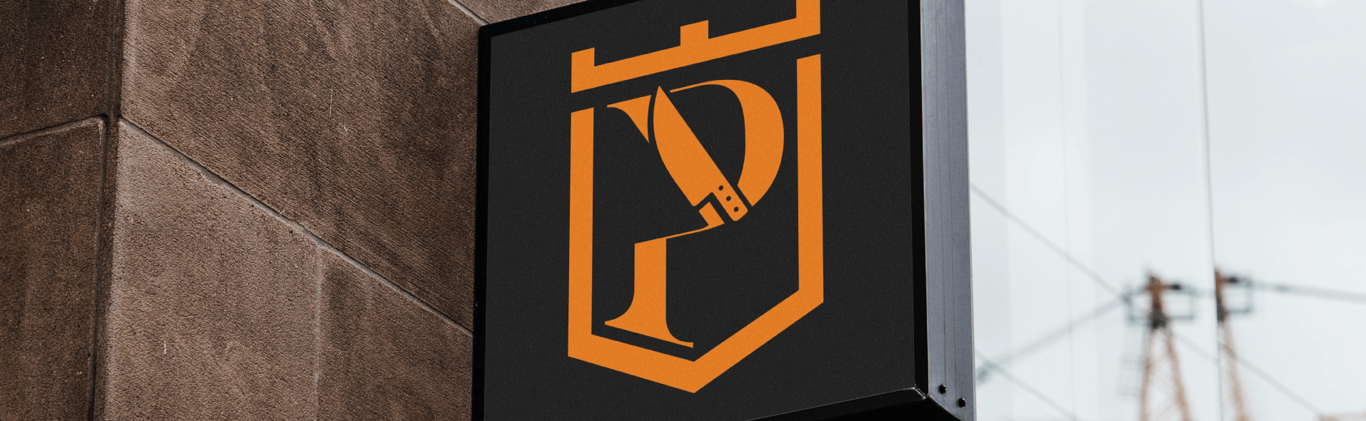 Placa com uma letra P laranja e um logotipo de faca em um fundo preto, fixada em uma parede de tijolos.